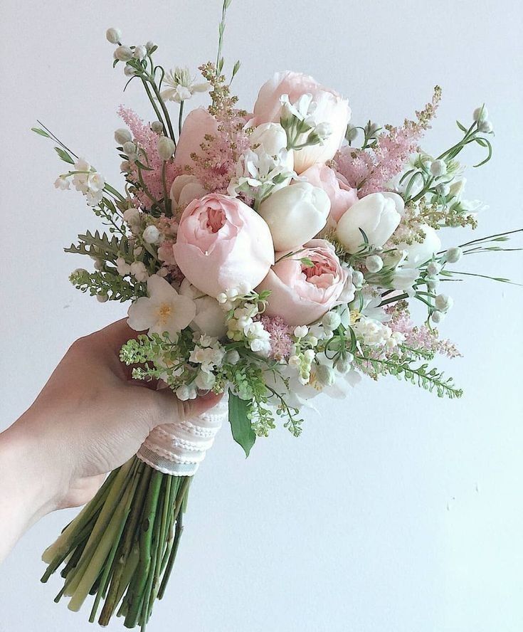 a person holding a bouquet of flowers in their hand with white and pink flowers on it