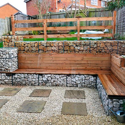 a wooden bench sitting on top of a gravel covered ground next to a stone wall