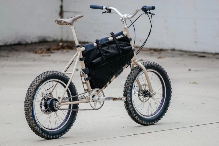 a bicycle with a black bag on the front wheel and handlebars is parked outside