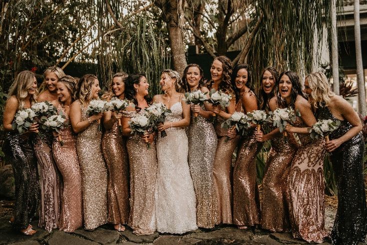 a group of women standing next to each other in front of trees and bushes holding bouquets