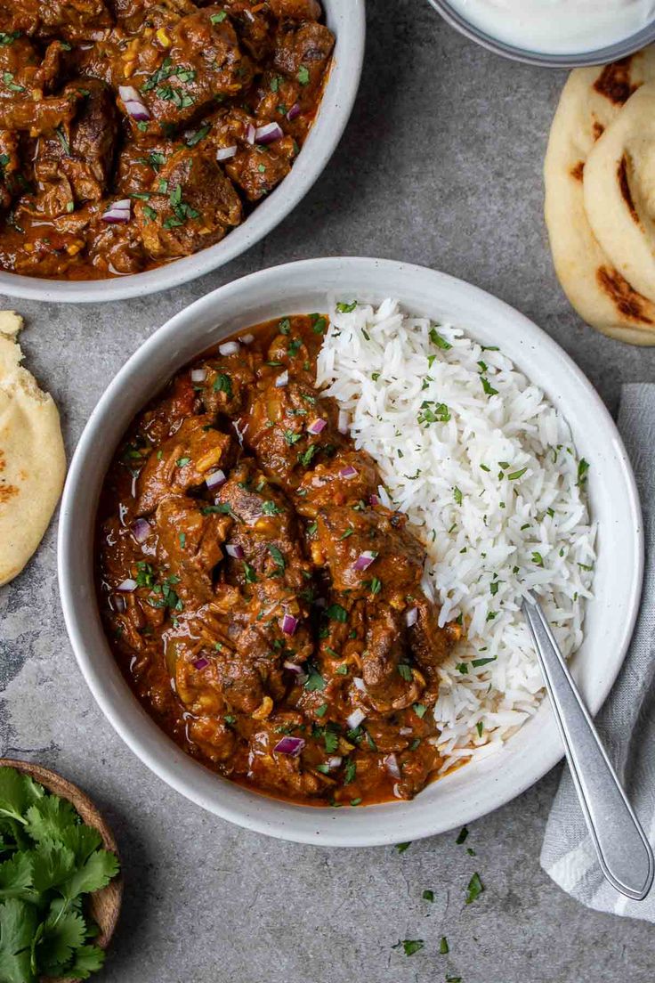 two bowls filled with meat and rice next to pita bread on a table top