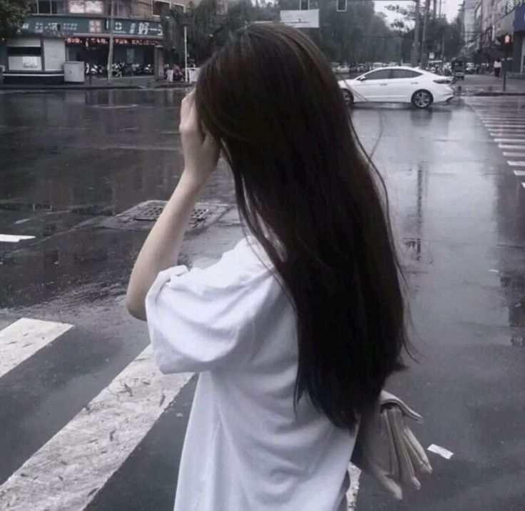 a woman standing on the side of a road holding an umbrella over her head and covering her eyes