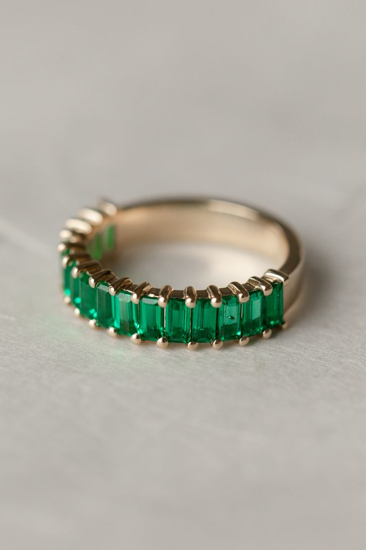 a gold band with emerald colored stones on the inside and outside, sitting on a white surface