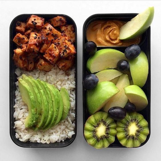 two black trays filled with rice and fruit next to each other on top of a white table