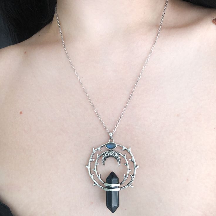 Thorns tell the beholder to love a beauty but from a safe distance. For if they come to pluck her beauty she will scratch back. Our magical circle of thorns hold a protective obsidian stone with a floating crescent moon above it under a labradorite stone. Labradorites enhance intuition. Our chain is 18" long with a 3" extension for additional length. Recycled brass base with a darker silver finish. Stones are genuine gemstone. All orders over $50 ship for free within the USA. All orders usually Black Metal Moon Shaped Jewelry, Black Crescent Metal Jewelry, Black Metal Moon-shaped Jewelry, Black Metal Crescent Jewelry, Mystical Round Pendant Metal Jewelry, Mystical Metal Round Pendant Jewelry, Spiritual Round Crystal Necklaces With Moon Phase, Black Moon Phase Jewelry For Festivals, Black Mystical Jewelry With Moon Charm