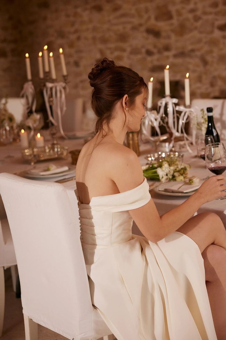 a woman sitting at a table with a glass of wine in her hand and looking down