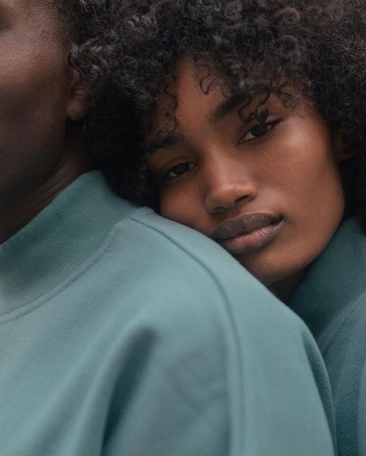 a close up of a person with curly hair wearing a blue sweatshirt and looking at the camera