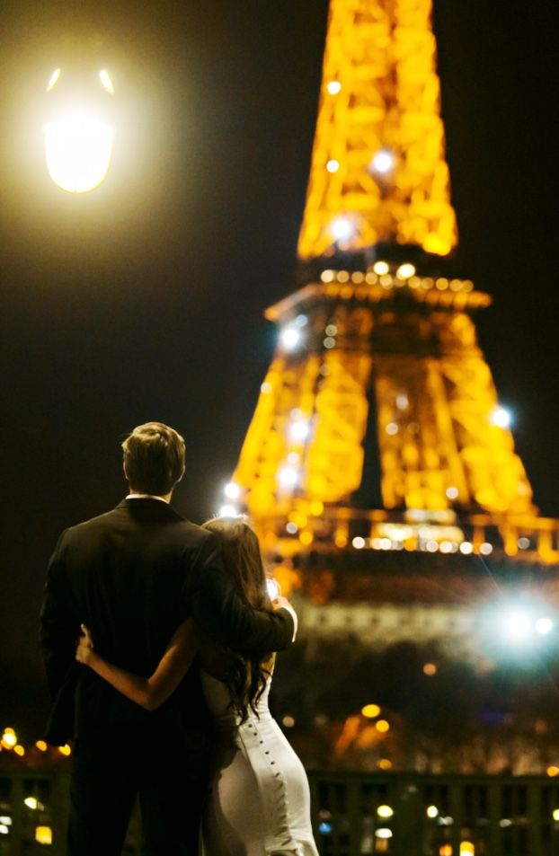 a bride and groom standing in front of the eiffel tower at night with their arms around each other