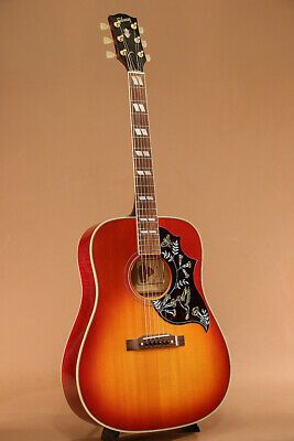 an acoustic guitar sitting on top of a wooden stand in front of a beige background