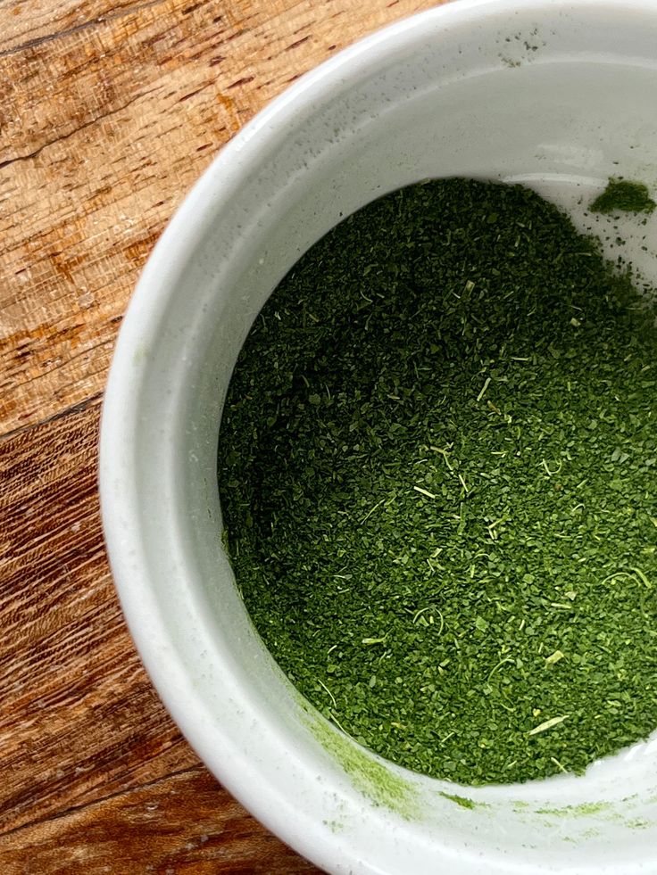 a white bowl filled with green stuff on top of a wooden table