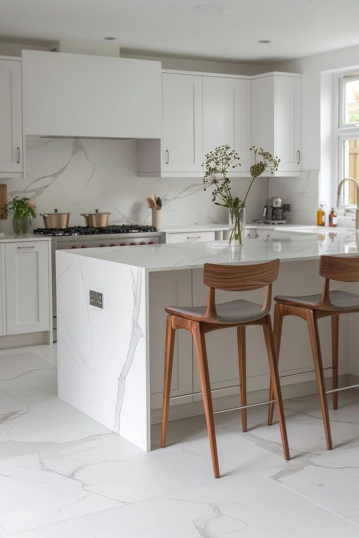 two wooden chairs sitting in front of a white kitchen island with marble counter tops and cabinets