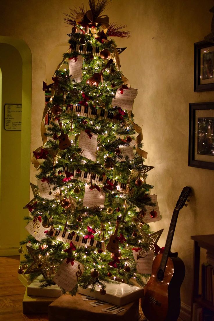 a christmas tree decorated with ribbons and lights in a living room next to a guitar