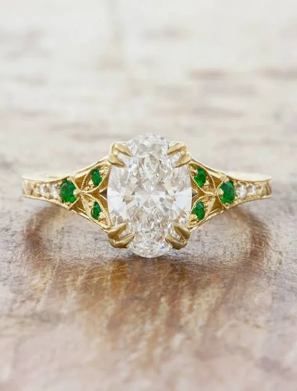 an oval diamond and emerald ring on a wooden surface