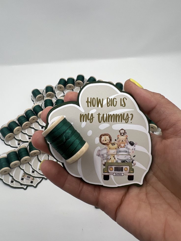 a hand holding a green spool of thread and a button with the words how big is my tummy?