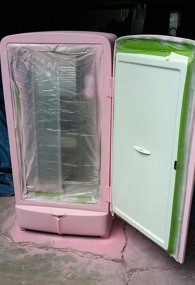 an open pink refrigerator sitting on top of a cement floor next to a plastic bag