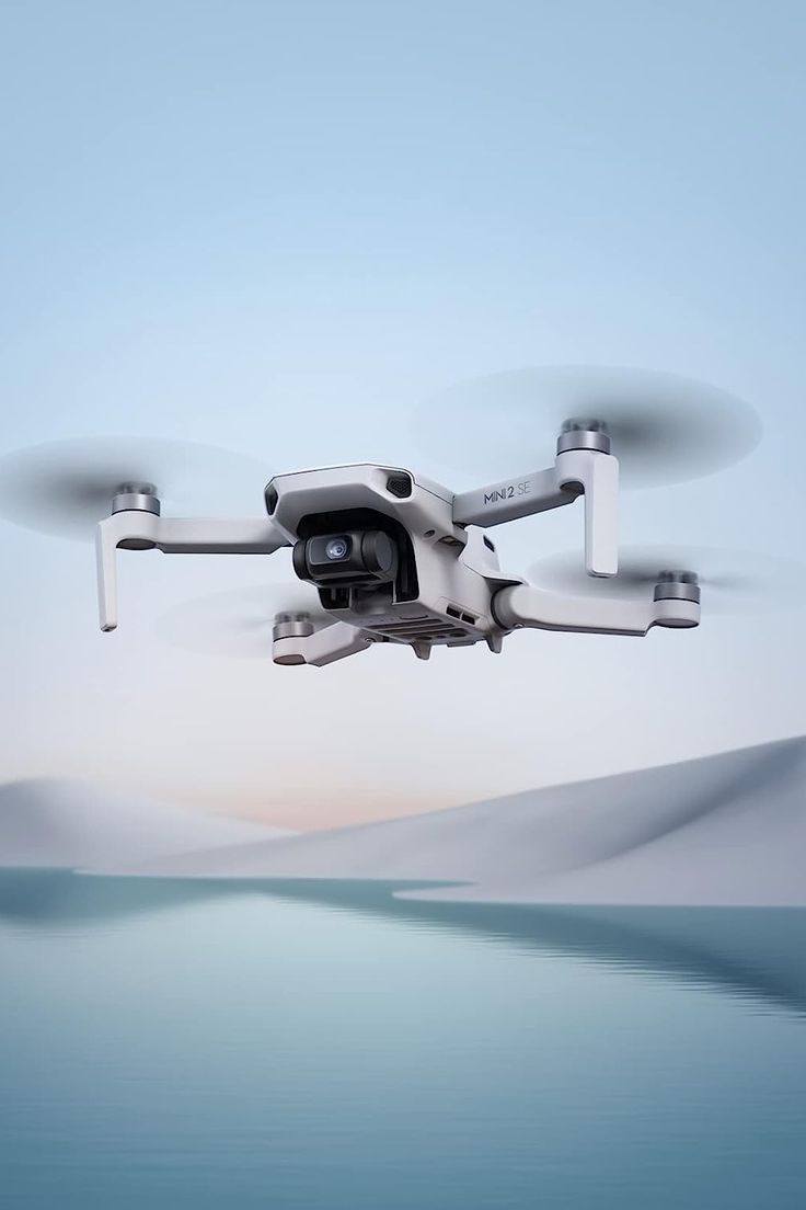 a white and black remote control flying over the ocean with sand dunes in the background