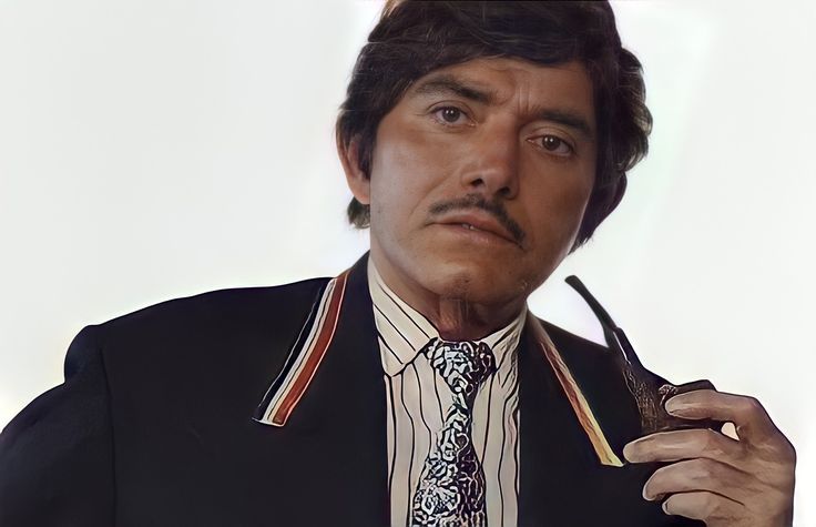 a man wearing a suit and tie holding a pipe in his right hand while looking at the camera