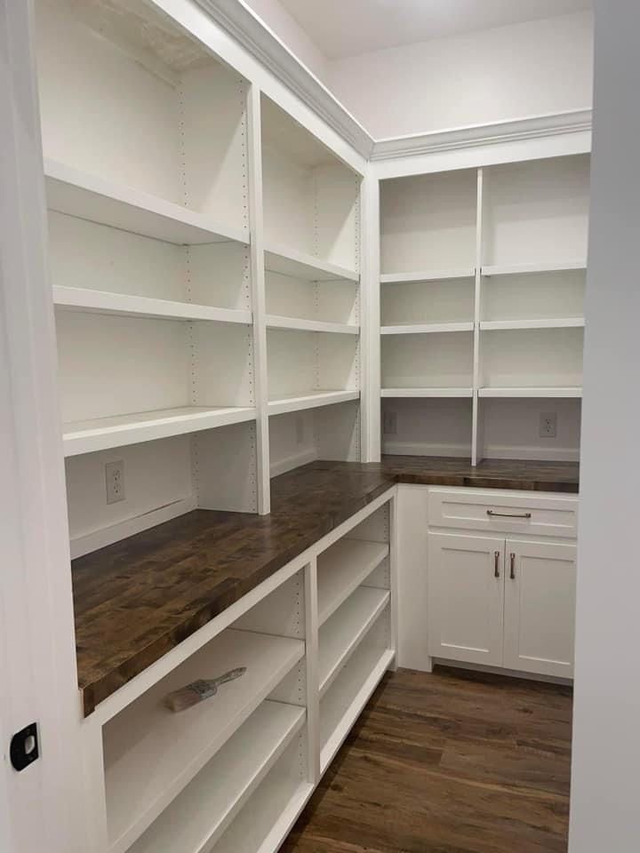 an empty walk in closet with white shelving and wood counter tops on the shelves