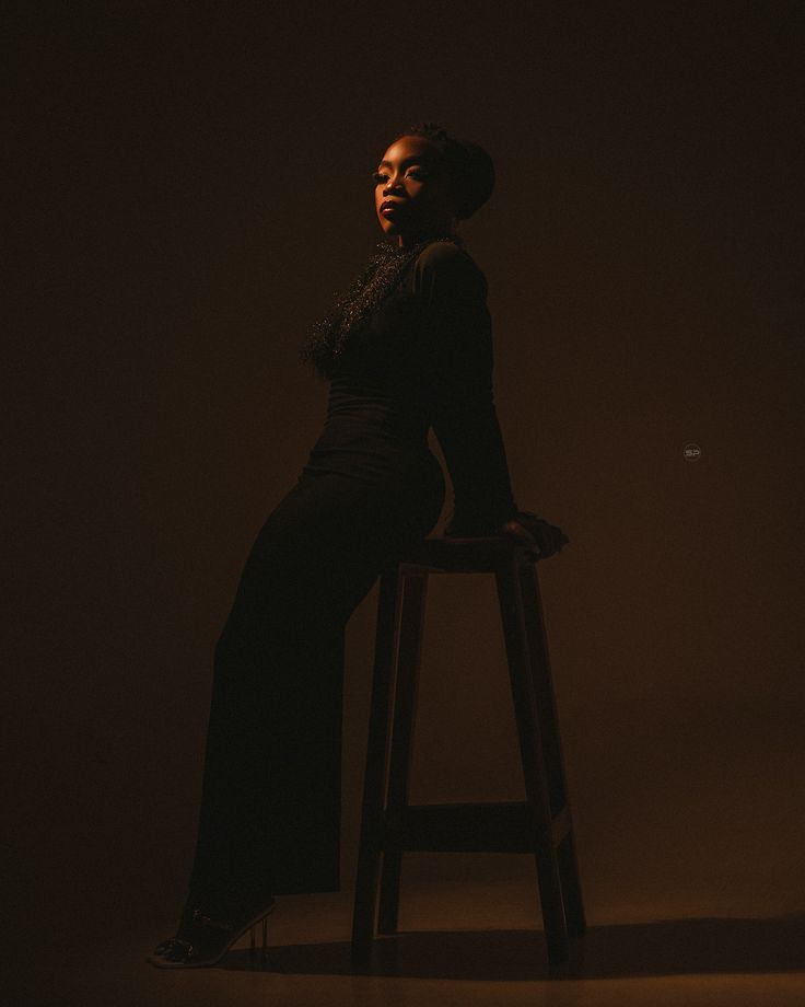 a woman sitting on top of a wooden stool in a dark room with her eyes closed