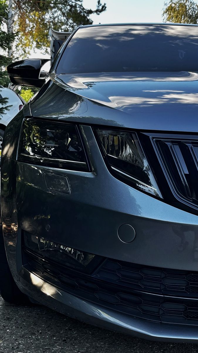 the front end of a black car parked in a lot with trees and bushes behind it