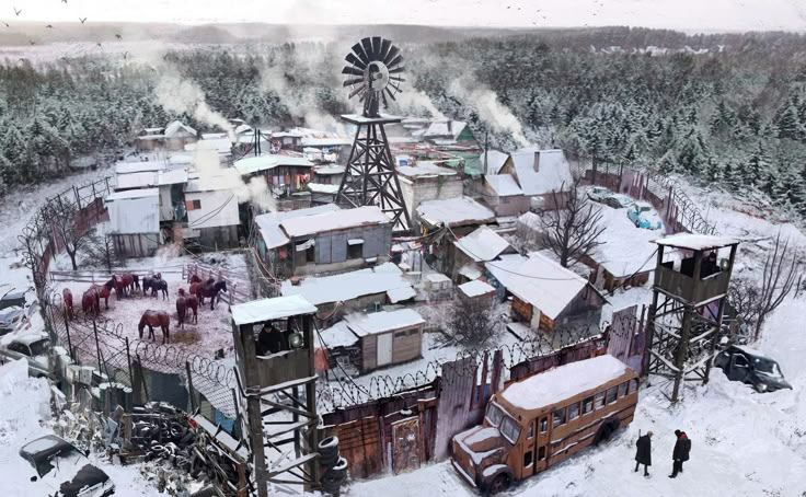 an aerial view of a snow covered town with horses in the foreground and people walking around