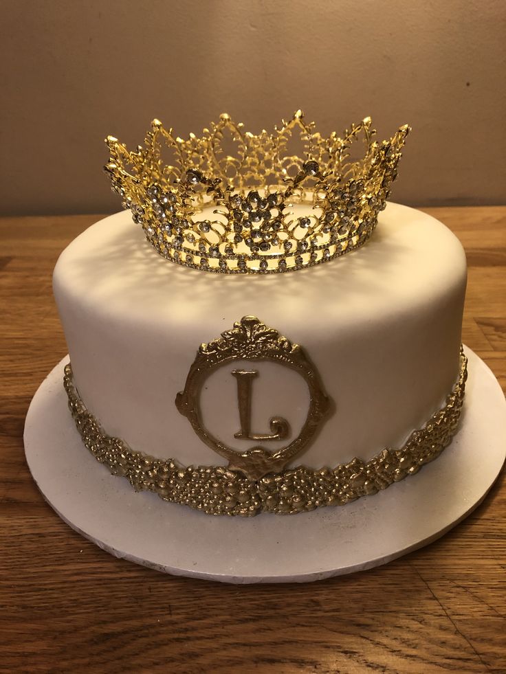 a white cake with gold decorations and a crown on top is sitting on a wooden table