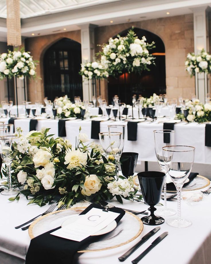 the table is set with white flowers and black place settings for an elegant wedding reception