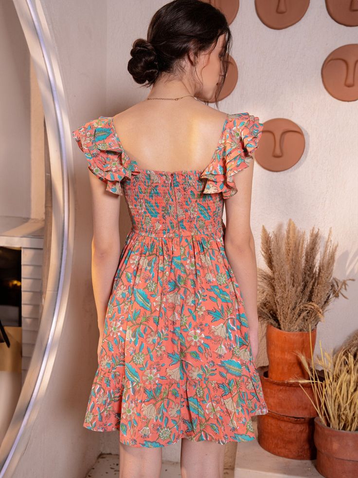 Just like the breeze, this fun short ruffle mini dress is a breath of fresh air. Crafted from 100% cotton cambric, it's as light and airy as a summer day. The floral jaal hand block print dances across the fabric, adding a touch of whimsy to its peach nectar hue. With its easy-to-wear fit & flare silhouette and charming balloon sleeves, this peach mini dress is perfect for casual occasions. Complete with a center-back zip closure and two pockets for practicality, it effortlessly combines style a Cotton Floral Sundress For Vacation, Summer Garden Party Ruffle Dress With Smocked Bodice, Flowy Cotton Floral Dress For Summer, Cotton Ruffled Mini Dress For Garden Party, Cotton Mini Dress With Ruffles For Garden Party, Tiered Cotton Mini Dress With Smocked Back, Summer Boho Dress With Floral Print, Knee-length, Bohemian Mini Sundress With Floral Print, Cotton Floral Sundress For Beach