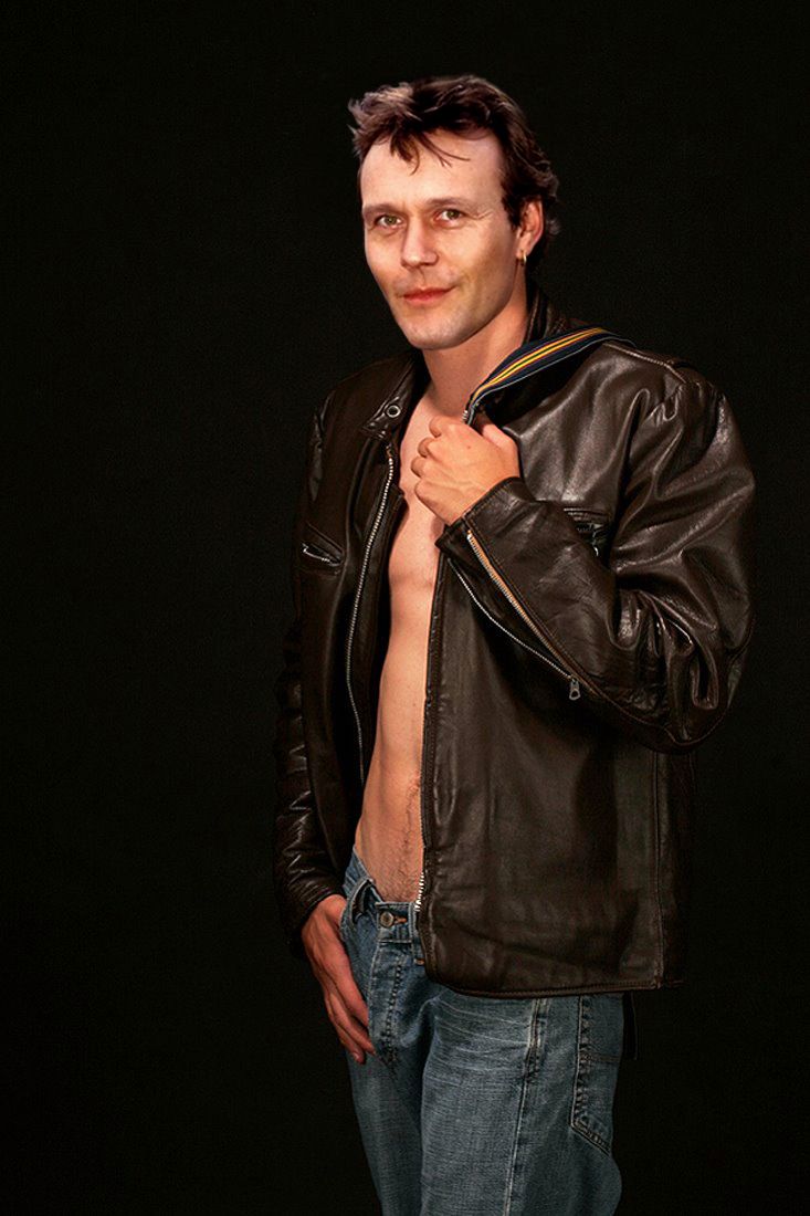 a man in jeans and a leather jacket posing for the camera with his shirt open