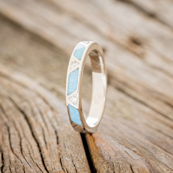 a wedding ring with blue and white designs on it sitting on a wooden surface in front of a piece of wood