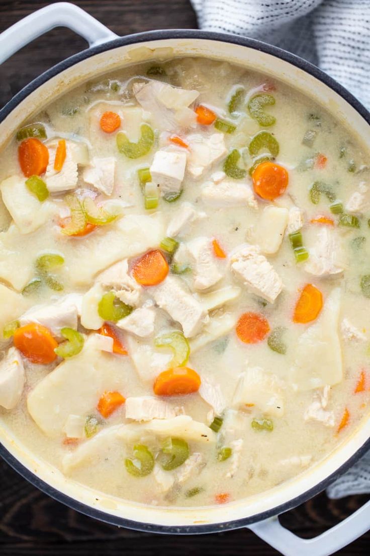 a pot filled with chicken, carrots and celery soup on top of a wooden table