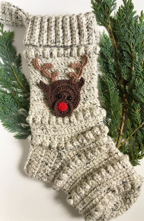 a crocheted christmas stocking with a reindeer head on it and pine needles