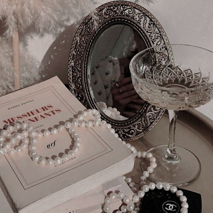 a table topped with a book, bracelets and a glass filled with liquid next to a mirror