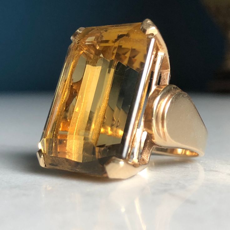 14k Stamped & tested yellow gold cast Citrine Quartz statement ring with a bright polish finish. This contemporary art-deco style fashion ring features a top center four- prong basket head-set emerald-shape step-cut citrine quartz with layered rolling cathedral shoulders. Ring measures approximately 20.00mm at the base of the top and approximately 9.50 wide at the wildest point of each shoulder tapering to approximately 2.78mm wide at the bottom of the shank. Ring size is: 5 3/4 Containing: One prong set emerald step cut natural citrine quartz. Measuring 24.00 x 17.50 x 11.66mm, (depth set). Approximate weight of 35.17ct, Clarity is eye clean, medium light, moderately strong, organgy yellow color, very good cut. Total Weight of Colored Stones:  36.17ct Total Weight of Ring:  16.28grams *20 Luxury Gold Faceted Rings, Luxury Yellow Gold Crystal Ring With Center Stone, Luxury Gold-tone Metal Ring, Luxury Yellow Gold Timeless Crystal Ring, Luxury Timeless Yellow Gold Crystal Ring, Luxury Yellow Gold Emerald-cut Crystal Ring, Luxury Faceted Yellow Gold Rings, Citrine Ring Engagement, Dream Rings