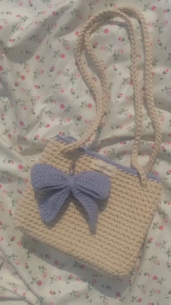 a crocheted purse with a blue bow on the handle sitting on a bed