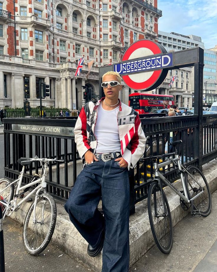 a man standing in front of a london sign with his hands on his hips while leaning against a fence