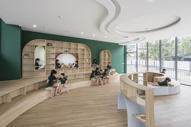 children are sitting on the floor in front of bookshelves and shelves with green walls