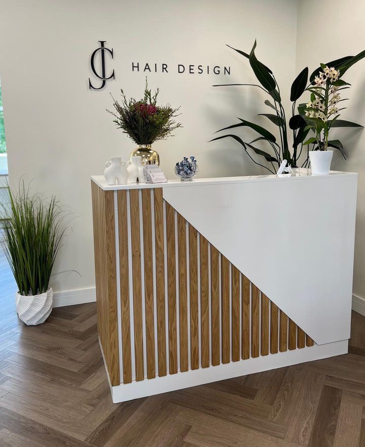 the front desk of a hair salon with plants and vases on it's sides