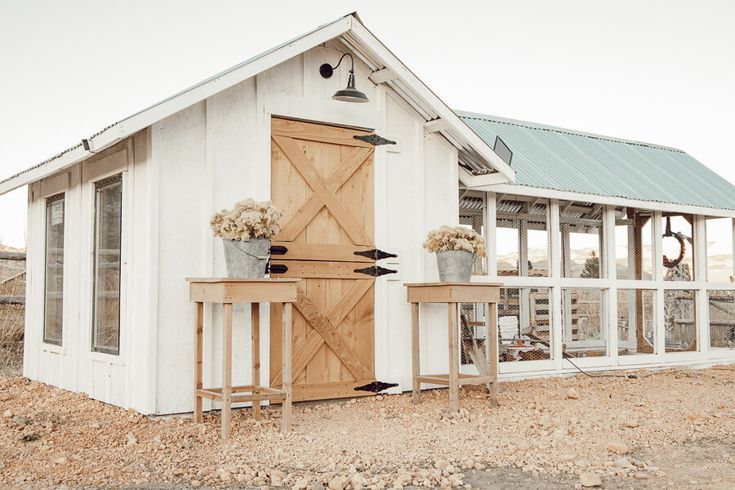 a small white shed with two planters on the outside and a table in front