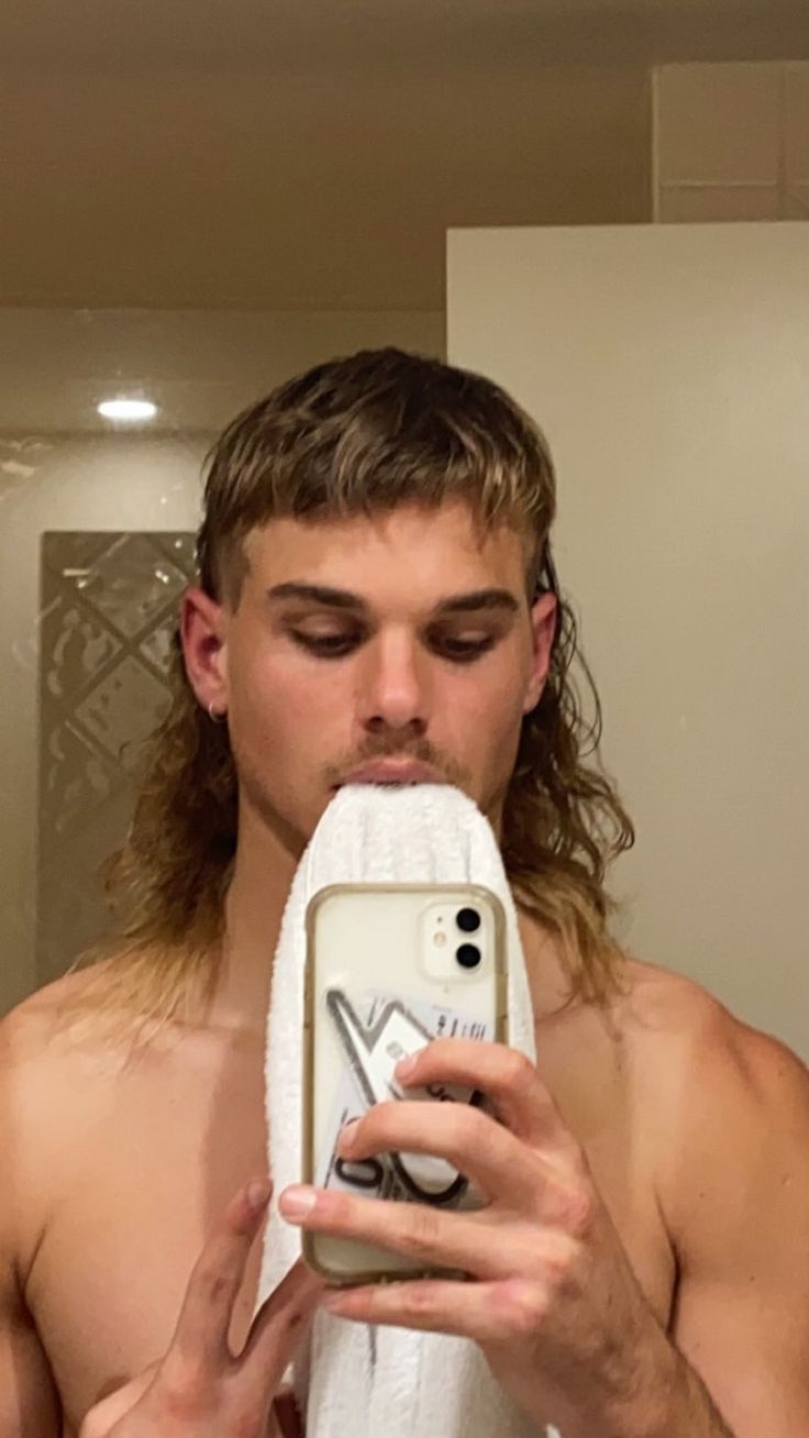 a man with long hair is taking a selfie in the mirror while holding a cell phone