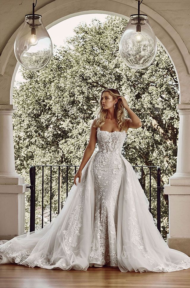 a woman in a white wedding dress standing on a porch with two lights hanging from the ceiling