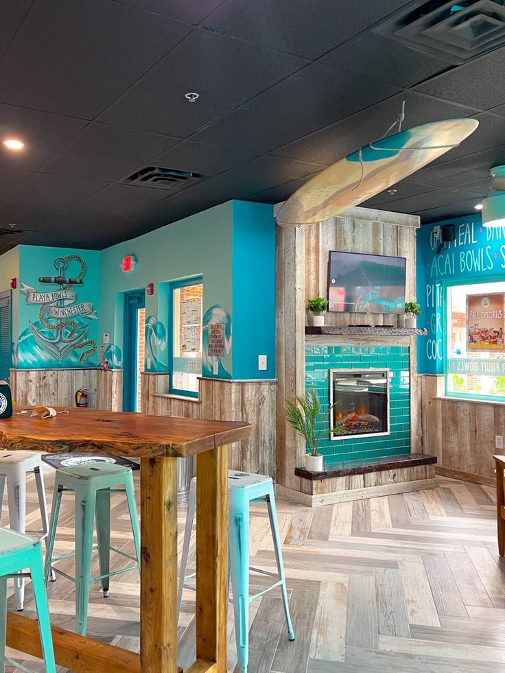 the inside of a restaurant with blue walls and wooden tables, chairs, and surfboards