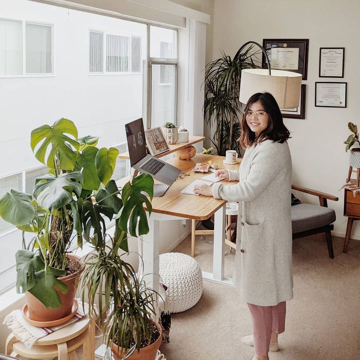 a woman standing in front of a desk with a laptop computer on top of it