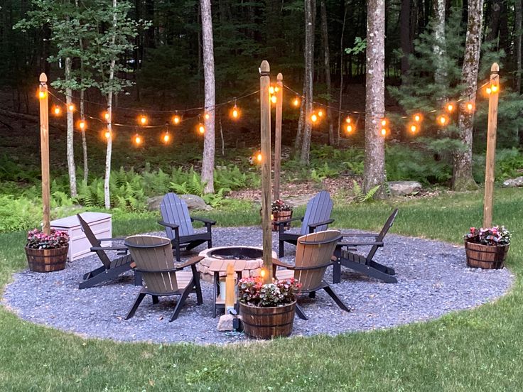 a fire pit surrounded by chairs and lights in the middle of a yard with lots of trees