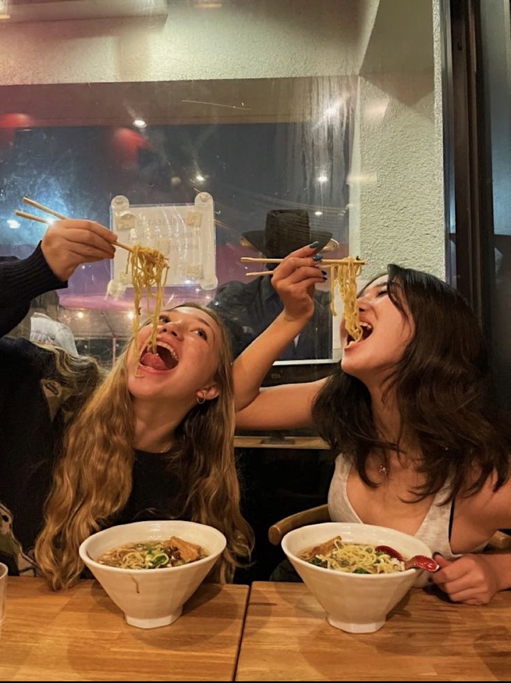 two women eating noodles with chopsticks at a restaurant