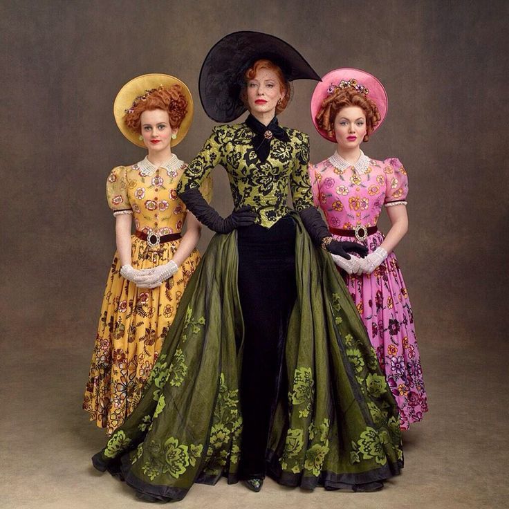 three women in dresses and hats posing for a photo