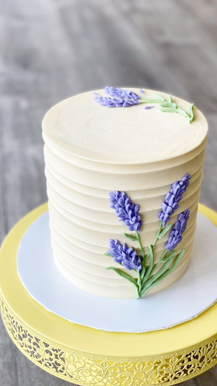 there is a white cake with purple flowers on the top and yellow trim around it