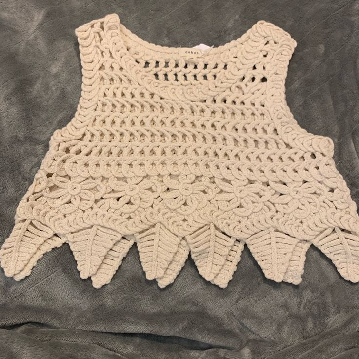 a crocheted top is laying on a gray surface, with the bottom part missing