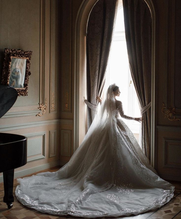 a woman in a wedding dress standing by a window