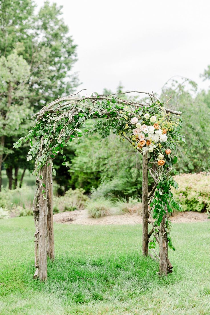 a wooden arch with flowers and greenery on it in the middle of a field